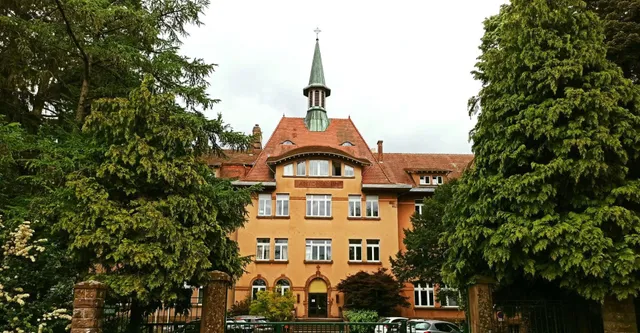 Das Gebäude des Lycée Saint Antoine mit einem auffälligen Turm steht umgeben von grünen Bäumen.