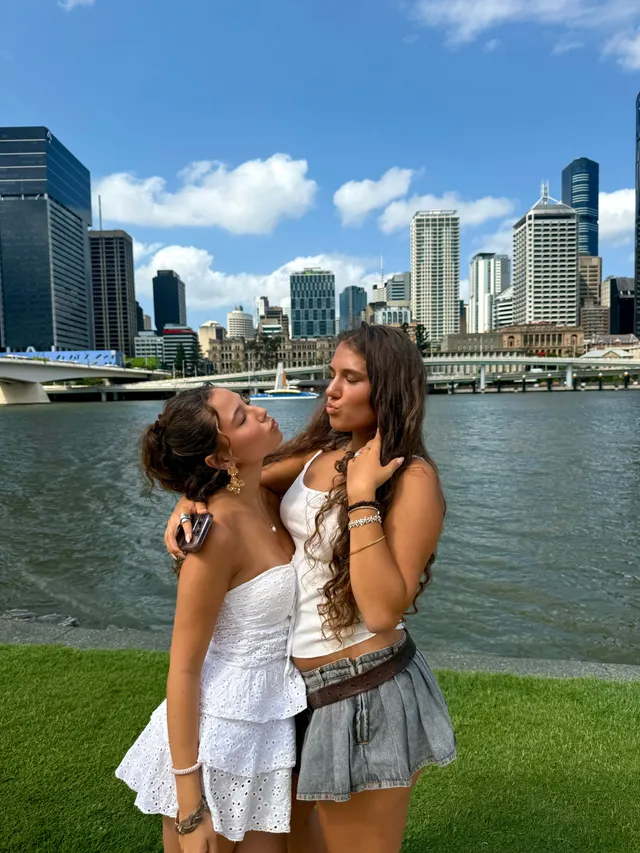 Dos chicas posando junto al río con los rascacielos de la ciudad al fondo