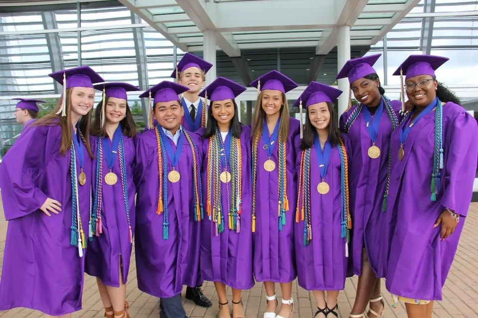 Un gruppo di neodiplomati in toghe viola si trova davanti a un edificio in vetro nel campus del Virginia Beach City Public School District.