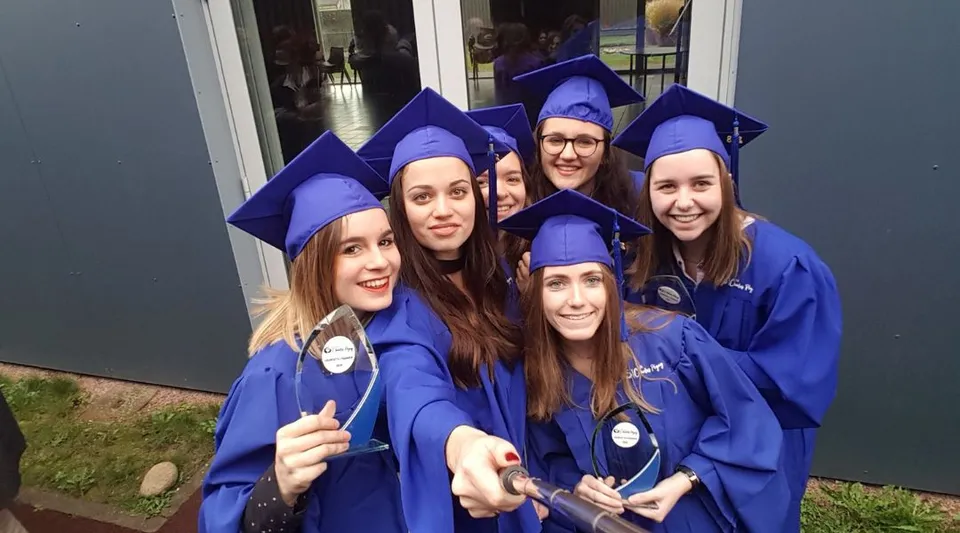 Un gruppo di giovani donne in toghe blu da diploma posa davanti a un edificio nel campus del Lycée Charles Péguy.