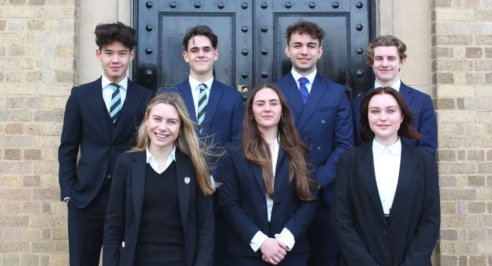 Sette studenti della Repton School in abito formale posano davanti a un portone di legno scuro.