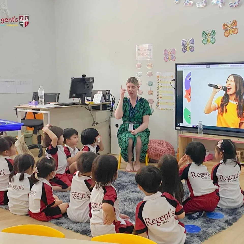 Eine Lehrerin sitzt im Klassenzimmer der Regent's International School Bangkok vor einer Gruppe von Kindern auf einem Teppich.