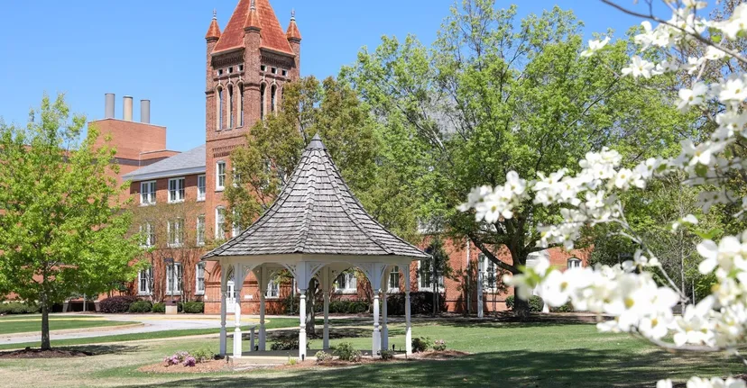 Un gazebo bianco nel campus della Lander University davanti a un edificio in mattoni con una torre.