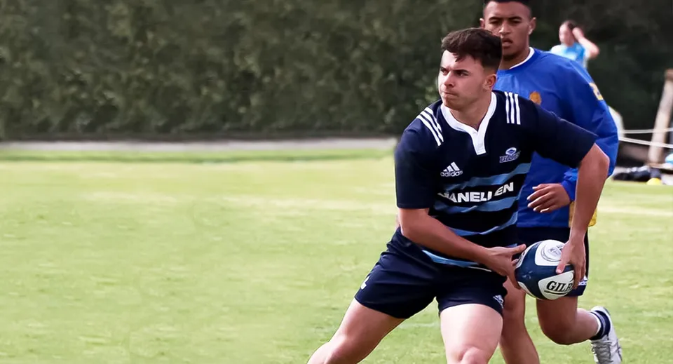 Uno studente della Mount Albert Grammar tiene un pallone da rugby su un campo erboso.
