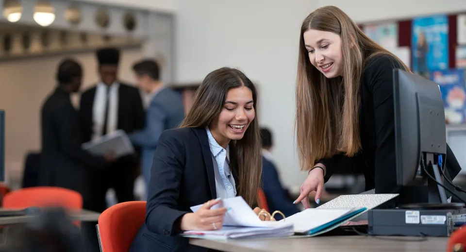 Due studentesse del Tettenhall College discutono insieme di alcuni documenti in un contesto professionale.