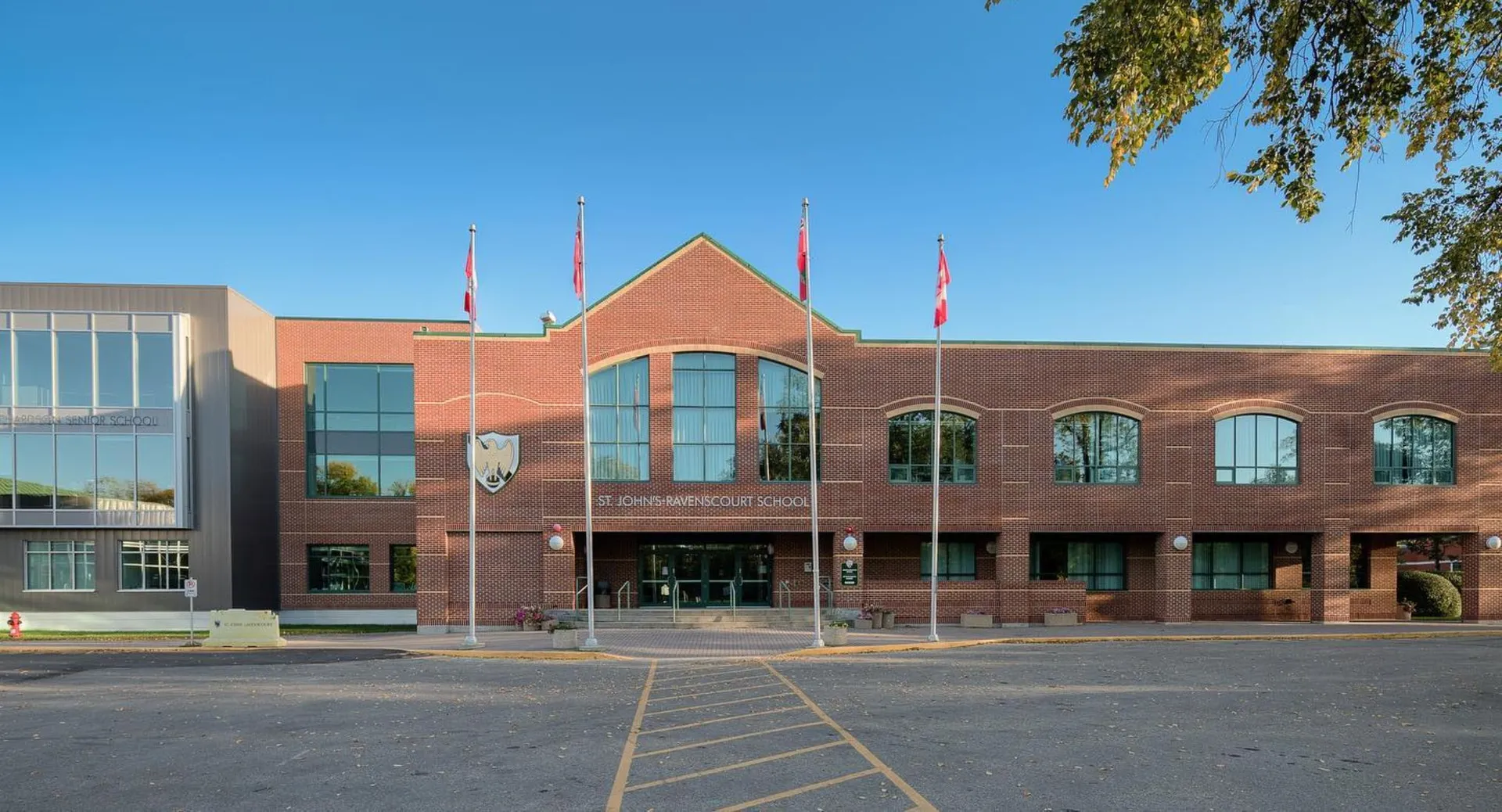 L'ampio edificio in mattoni con finestre ad arco nel campus della St. John’s-Ravenscourt School è circondato da un'area pavimentata e da alberi.