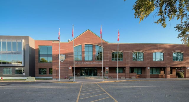 El gran edificio de ladrillo con ventanas de arco en el campus de St. John’s-Ravenscourt School está rodeado por una zona pavimentada y árboles.