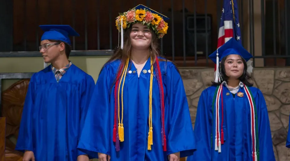 Tre studentesse della Hawaiian Mission Academy in toga blu da diploma davanti a un edificio in pietra.