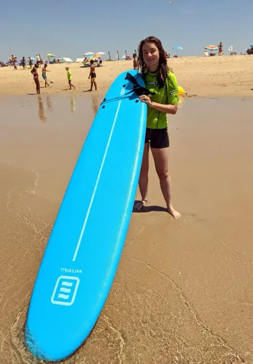 Ragazza in muta con una tavola da surf azzurra su una spiaggia affollata