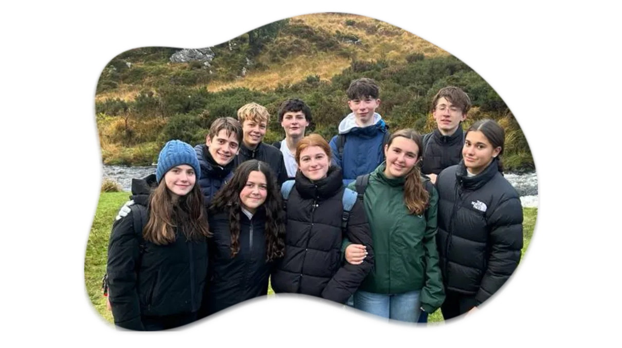 Grupo de estudiantes de intercambio con chaquetas de abrigo sonríe ante un arroyo y una colina verde del paisaje irlandés