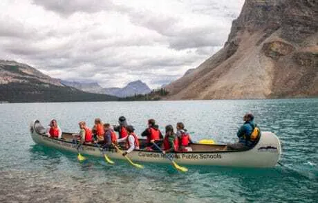 Grupo de jóvenes remando en canoa por un lago turquesa rodeado de grandes montañas