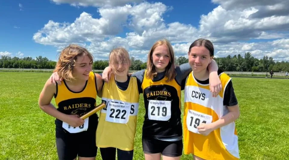 Quattro giovani atlete in maglia giallo-nera stanno sul campo sportivo della Cornwall Collegiate & Vocational School sotto un cielo nuvoloso.