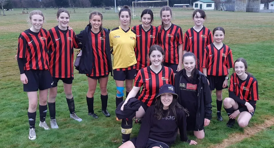 Una squadra di giovani calciatrici è in piedi insieme sul campo sportivo del James Hargest College davanti alla porta.