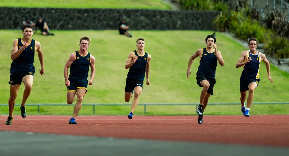 Un gruppo di atleti in divisa nera corre sulla pista da atletica della Auckland Grammar School.