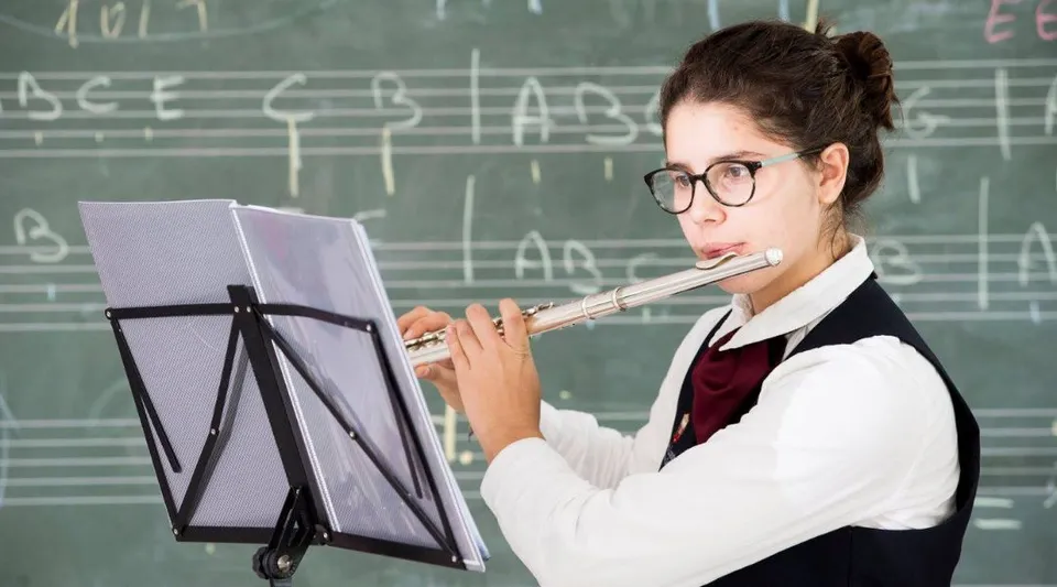 Una studentessa della North London Grammar School suona il flauto davanti a una lavagna.