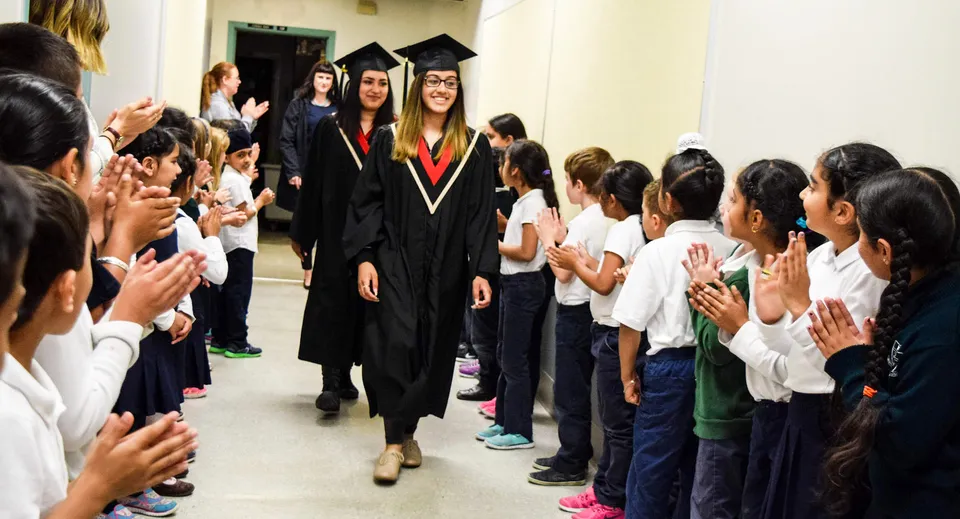 I diplomati della Abbotsford Traditional Secondary School camminano con le loro toghe lungo un corridoio pieno di studenti festanti.