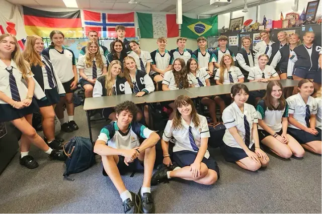 Studenti di una classe in posa davanti a una parete con bandiere internazionali