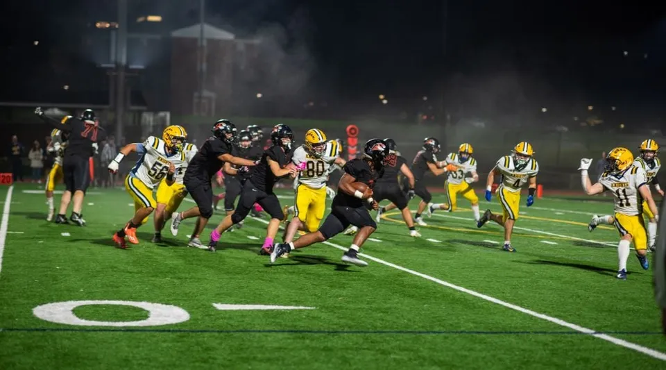 Studenti della Suffield Academy giocano una partita di football sul campo illuminato al crepuscolo.