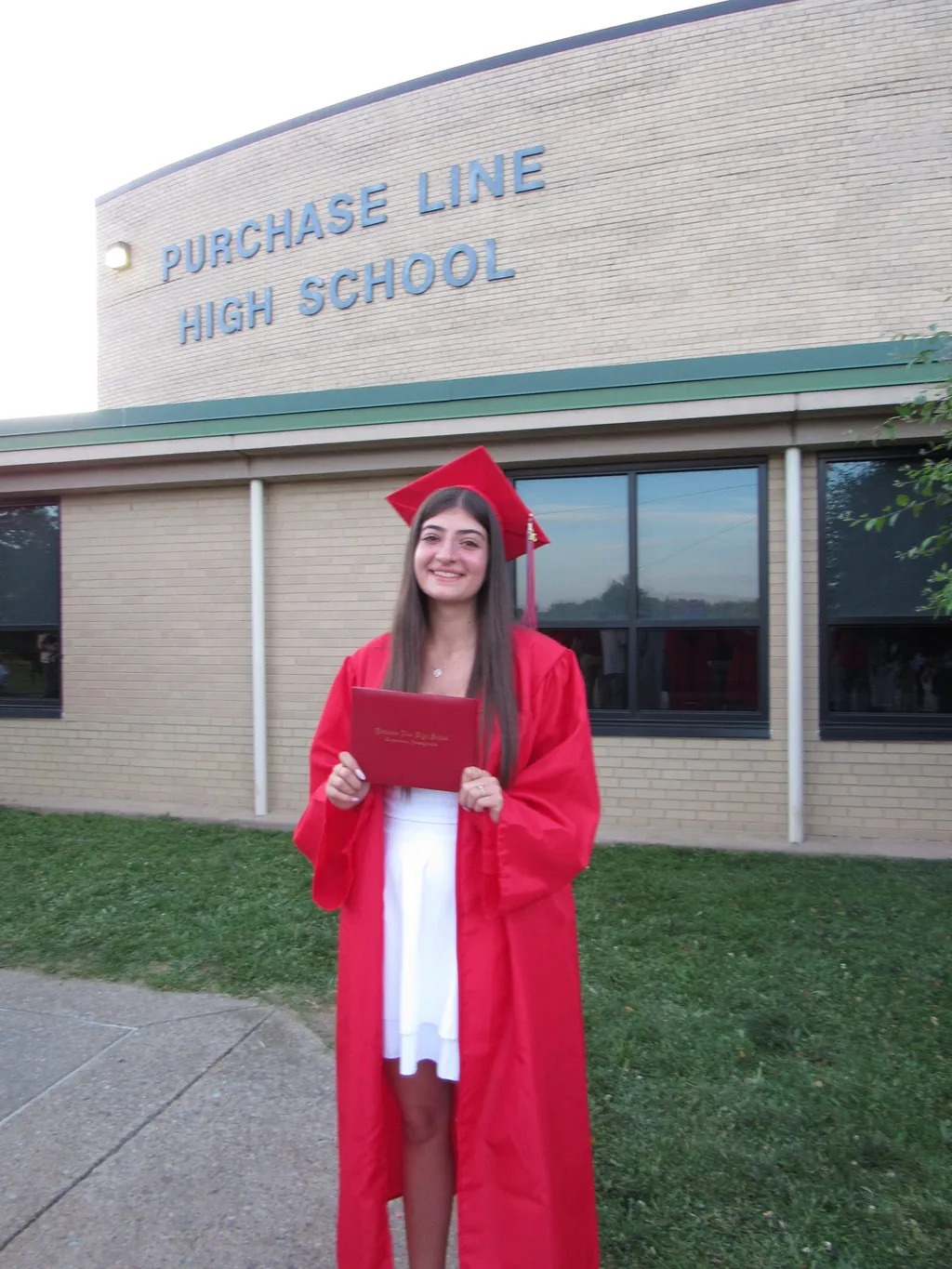 Francesca in toga e tocco rossi con il diploma davanti alla sua high school negli USA
