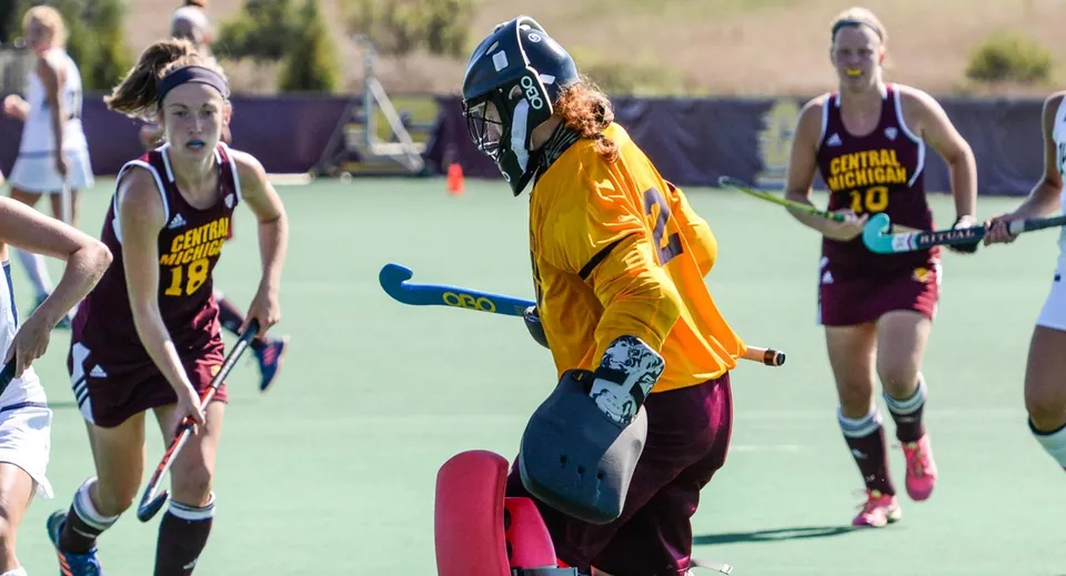 Studenti della Langley School giocano a hockey su prato sul campo sportivo con un giocatore in divisa gialla in primo piano.