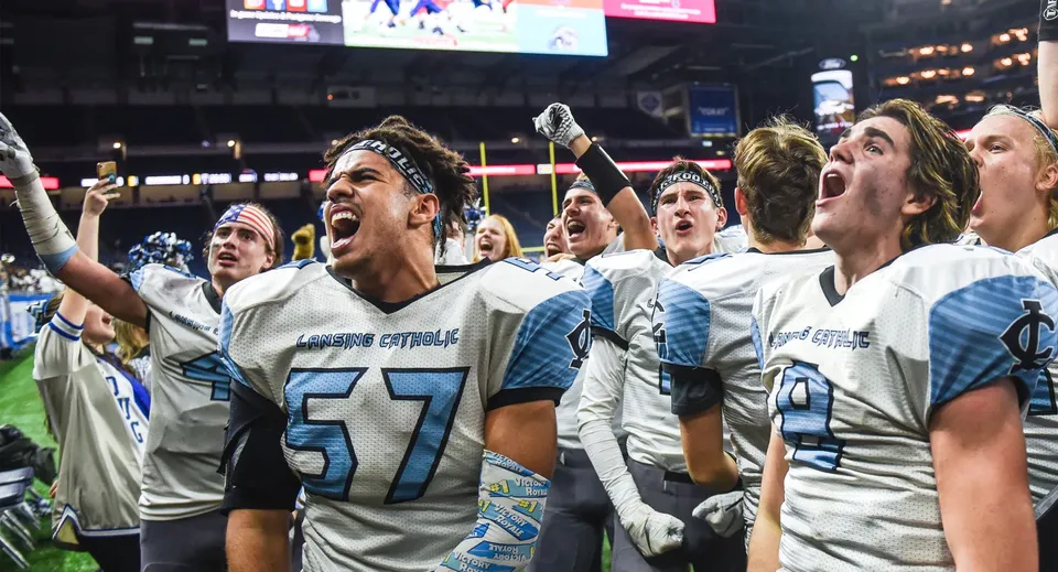Studenti della Lansing Catholic High School festeggiano insieme sul campo da football davanti al tabellone segnapunti e all'illuminazione dello stadio.