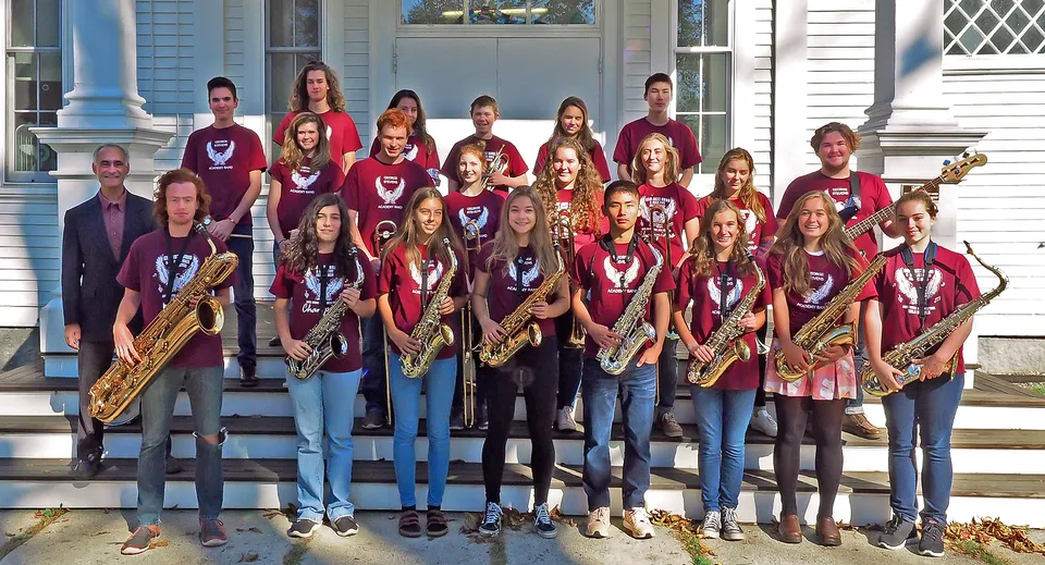 Studentesse della George Stevens Academy in uniforme rossa e con strumenti musicali stanno sulle scale di un edificio con colonne.