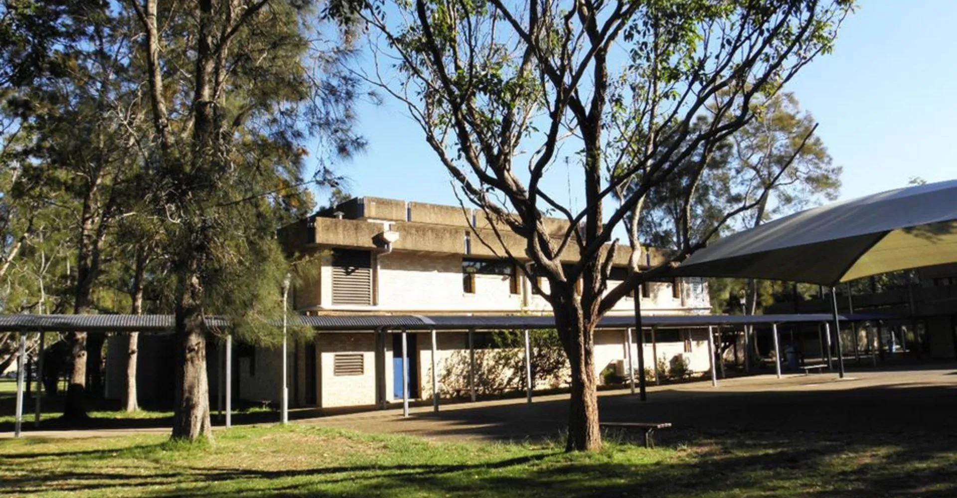 L'edificio a più piani della Narrabeen Sports High School è circondato dal verde e mostra un vialetto pavimentato con un'area sedute coperta.