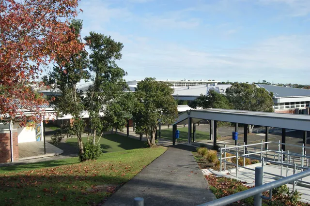 Das moderne Gebäude des Birkenhead College mit großen Fenstern und einem gepflegten Heckenrand unter blauem Himmel.