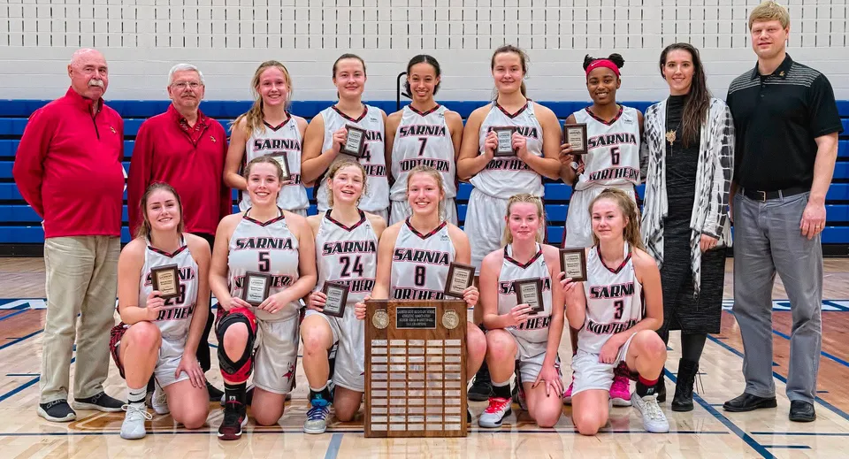 Un gruppo di giovani giocatrici di basket del Northern Collegiate Institute & Vocational School tiene insieme un trofeo in palestra.
