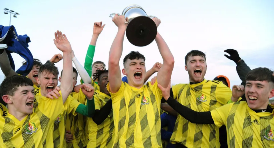 Un gruppo di giovani calciatori festeggia con una coppa sul campo da gioco della Douglas Community School.
