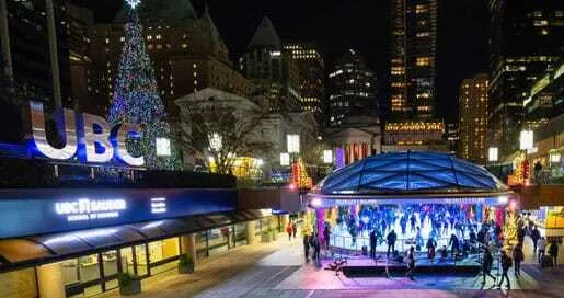 Plaza urbana de noche con pista de hielo iluminada, un gran árbol navideño y rascacielos
