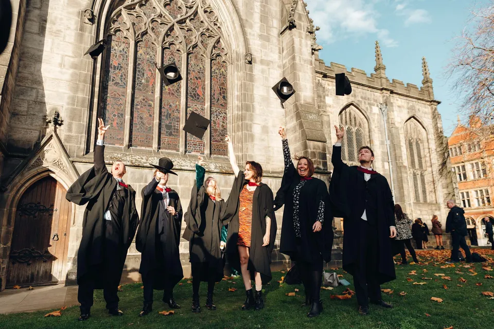 Un gruppo di diplomati e diplomate di The Sheffield College si trova davanti a una cattedrale gotica in autunno.