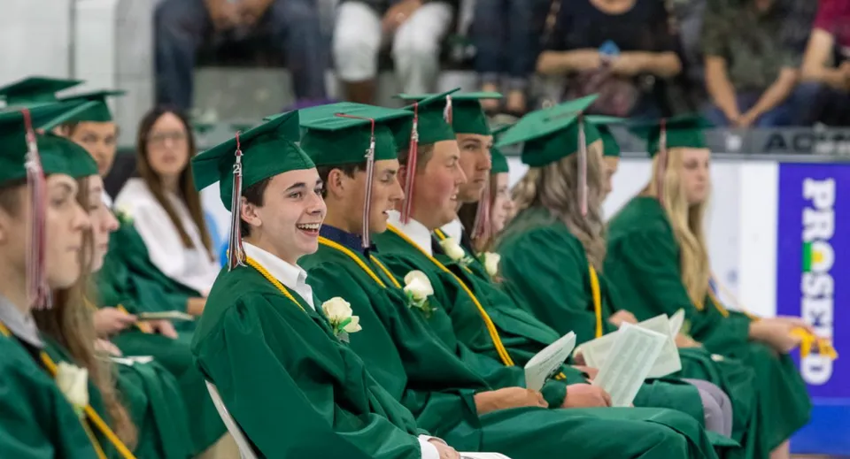 Un gruppo di diplomati della Craigslea State High School indossa toghe verdi e siede insieme alla cerimonia di diploma.