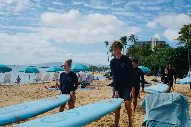 Estudiantes con neopreno y tablas de surf en una playa de Hawái con palmeras al fondo