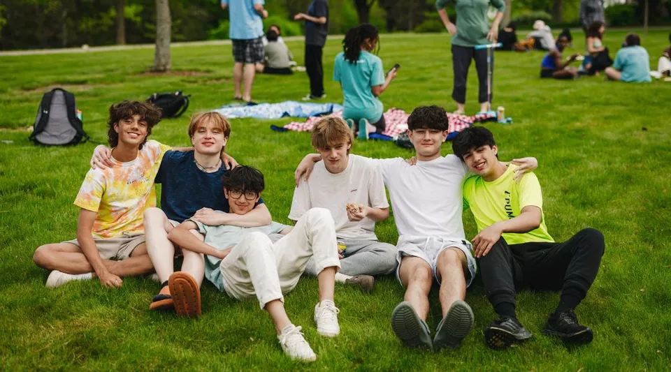 Un gruppo di studenti della Northfield Mount Hermon School è seduto insieme su un prato con alberi sullo sfondo.