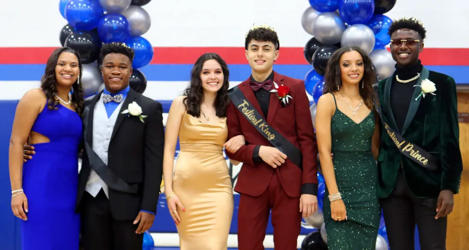 Un gruppo di persone in abiti formali posa davanti a palloncini blu e argento nel campus della Wisconsin Lutheran High School.