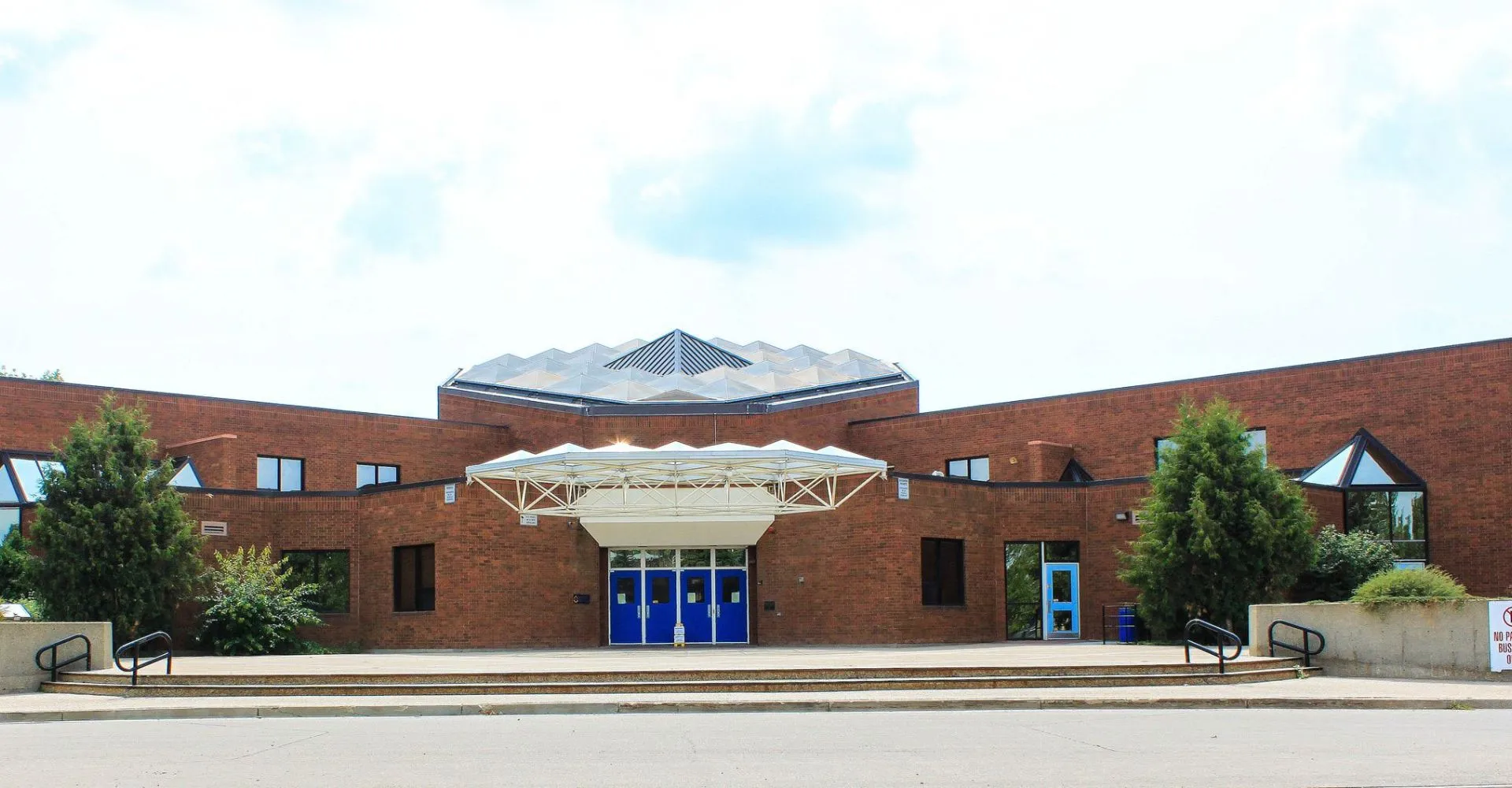 L'edificio moderno in mattoni della École Secondaire Beaumont Composite High School con tetto triangolare e ingresso in vetro circondato da alberi.