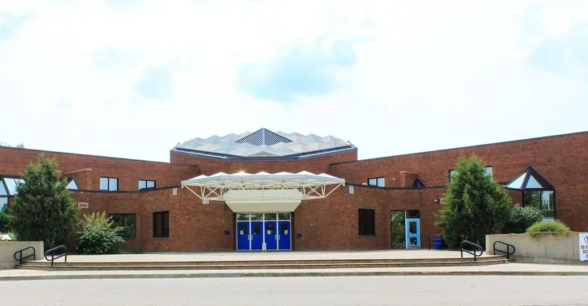 L'edificio moderno in mattoni della École Secondaire Beaumont Composite High School con tetto triangolare e ingresso in vetro circondato da alberi.