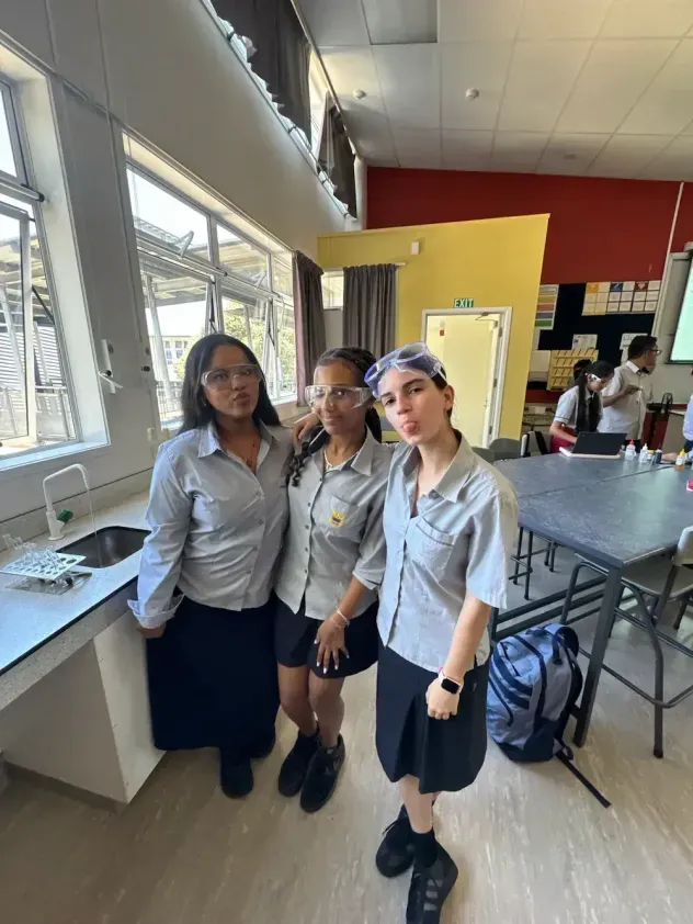 Tres alumnas con uniforme escolar y gafas de protección en un aula de ciencias en Nueva Zelanda