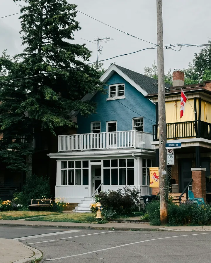 Blaues kanadisches Wohnhaus mit Veranda und kanadischer Flagge in einer ruhigen Wohnstraße