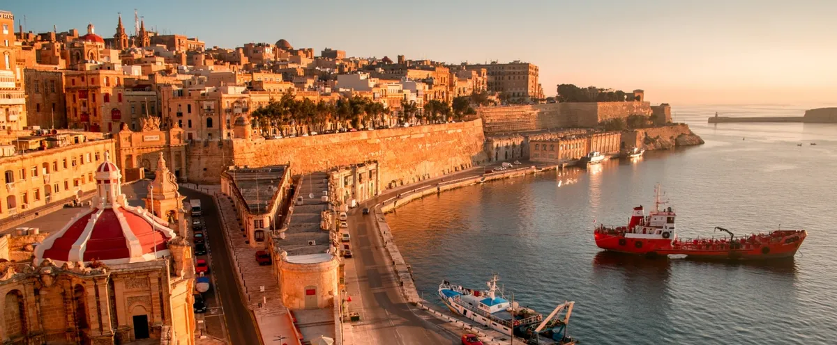 Vista desde arriba del Grand Harbour de La Valeta con las murallas de piedra dorada y un barco rojo