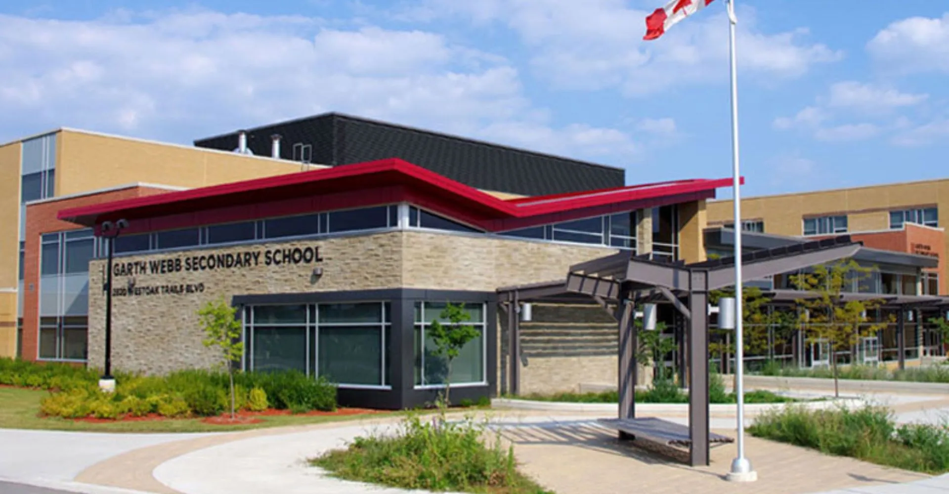 L'edificio moderno a più piani della Garth Webb Secondary School con tettoia rossa e bandiera canadese davanti.
