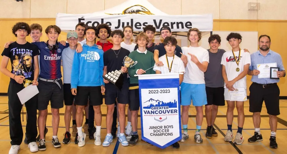 Un gruppo di studenti della Jules Verne school Vancouver posa nella palestra con uno striscione della scuola e una targa del campionato.