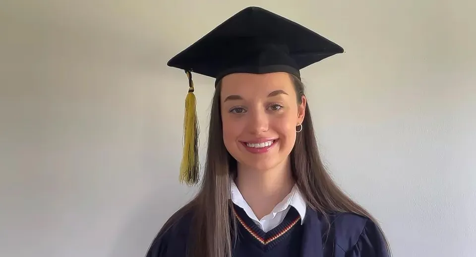 Una diplomata della St. Mary’s Secondary con tocco e toga da diploma su sfondo bianco.