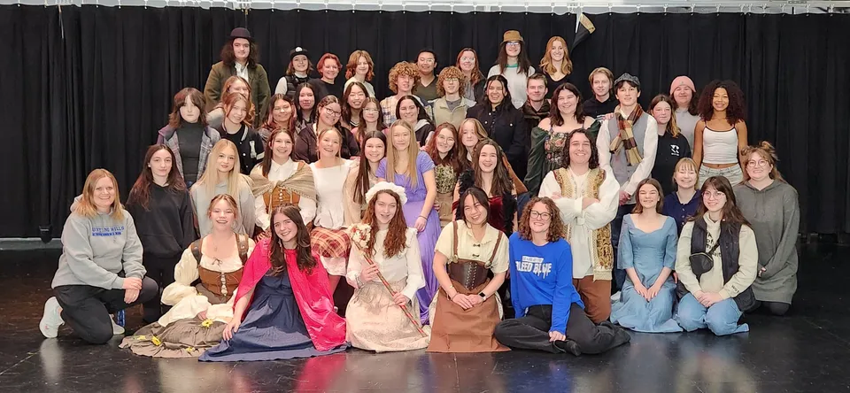 Un grande gruppo di donne si trova insieme sul palco della Hunting Hills High School davanti a un sipario nero.
