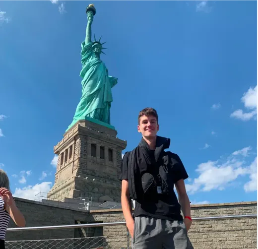 Ragazzo sorridente davanti alla Statua della Libertà a New York