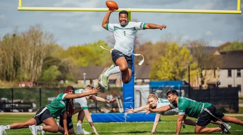 Un giocatore di football americano della University of Limerick salta in aria con un pallone davanti alla porta.