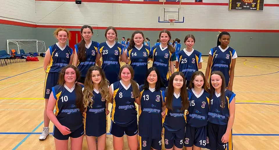 Un gruppo di giovani giocatrici di basket in maglia blu scuro posa sul campo da basket della St. Louis Secondary School.