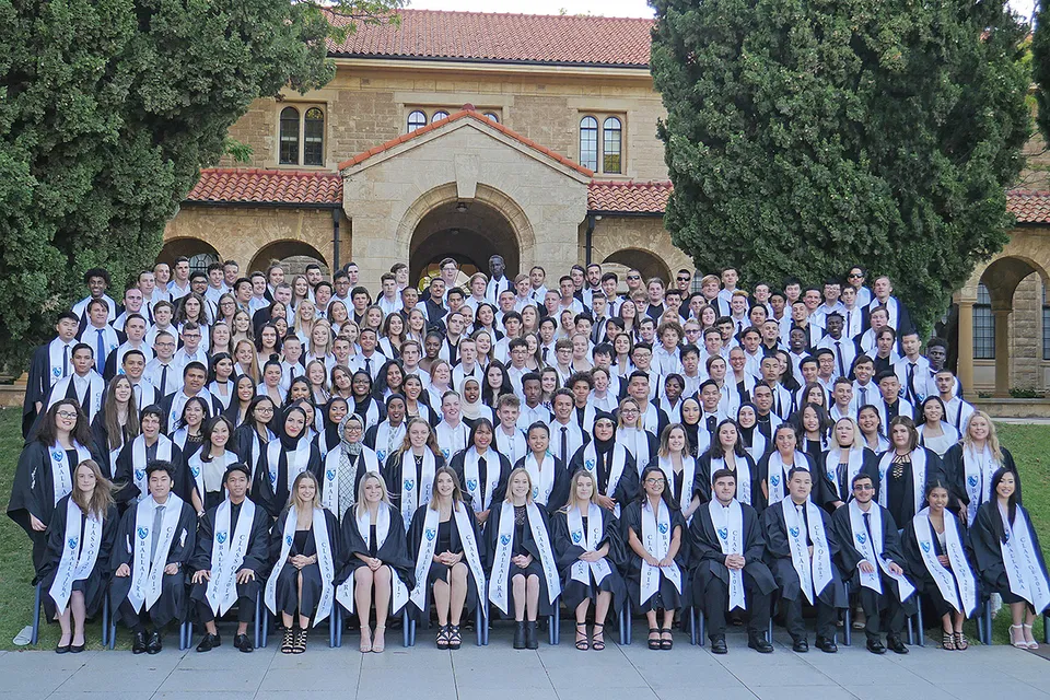 Un gruppo di studenti con l'abito da diploma si trova davanti a un edificio storico nel campus del Ballajura Community College.