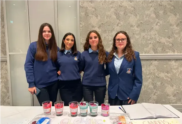 Cuatro estudiantes con uniforme detrás de un puesto de velas hechas a mano en Irlanda